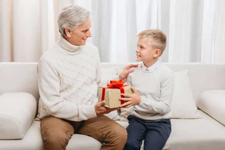 Grand-père et petit-garçon souriants avec un cadeau à la maison, transmission entre générations
