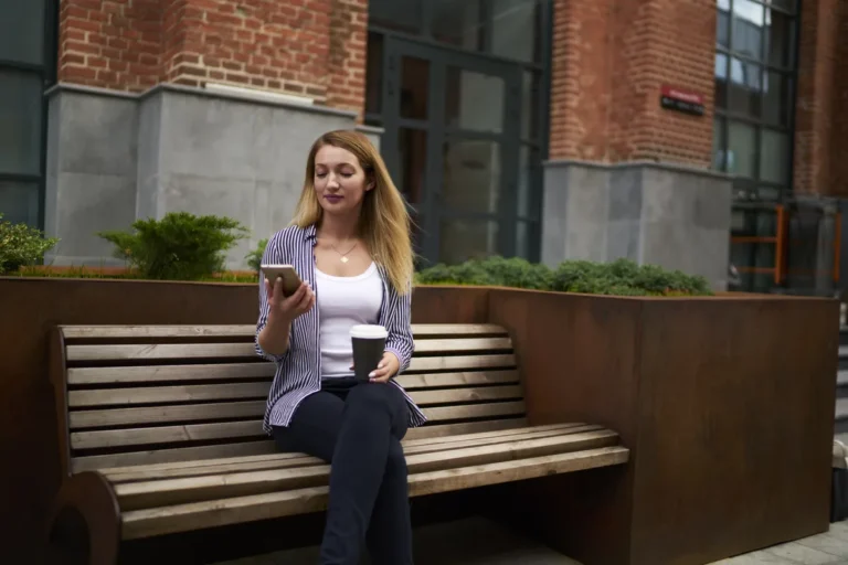 Femme assise sur un banc consultant son téléphone, un café à la main
