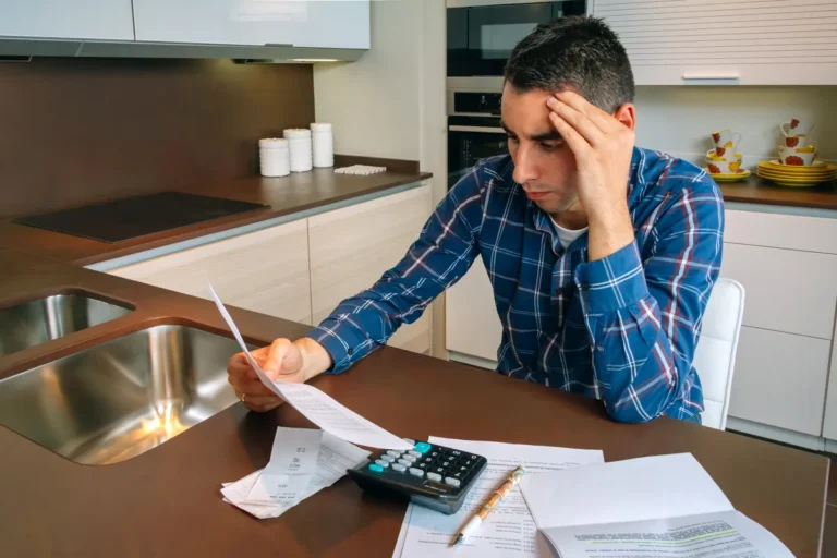 Homme soucieux faisant ses comptes avec une calculatrice à la table de la cuisine