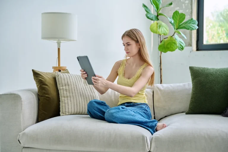 Jeune femme sur son canapé consultant sa banque en ligne sur tablette