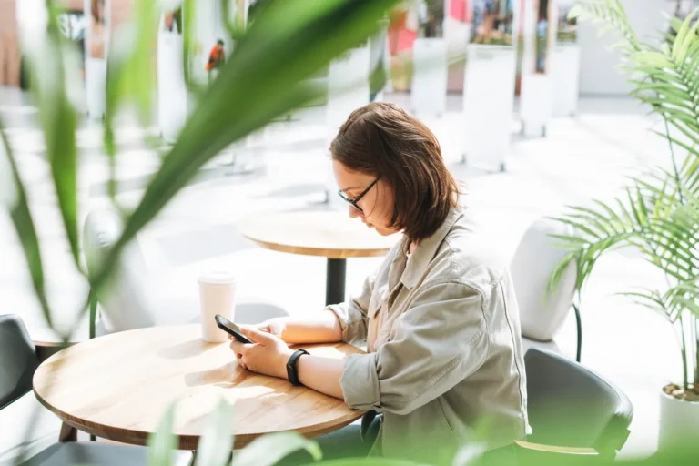 Femme consultant son smartphone dans un café entouré de plantes vertes