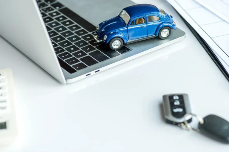 Voiture miniature posée sur un ordinateur portable et clés de voiture, assurance auto en ligne