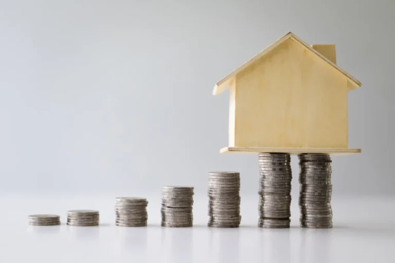 Maquette de maison en bois posée sur des piles de pièces, épargne pour un projet immobilier