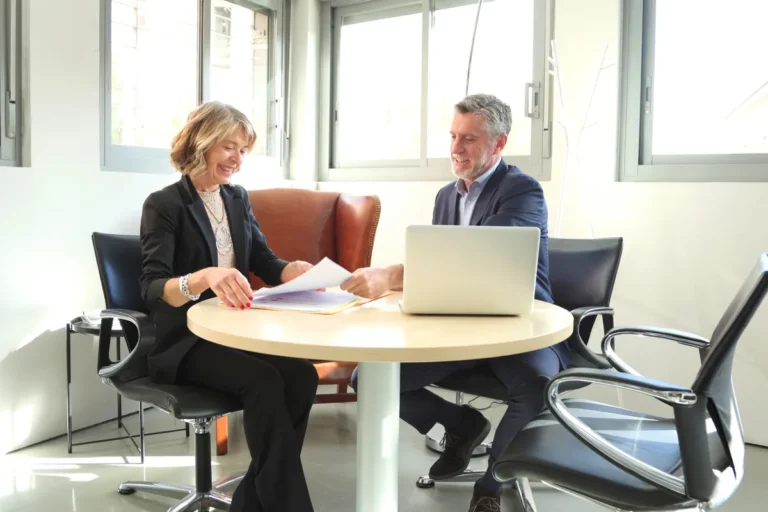 Femme et homme souriants passant en revue un document lors d'un rendez-vous au bureau