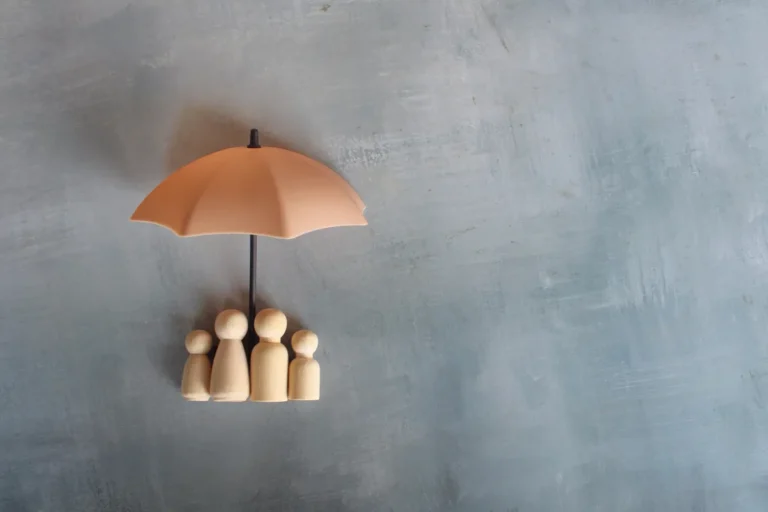 Figurines en bois d'une famille abritées sous un parapluie, symbole de protection par l'assurance