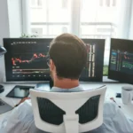 Trader de dos devant plusieurs écrans de graphiques boursiers
