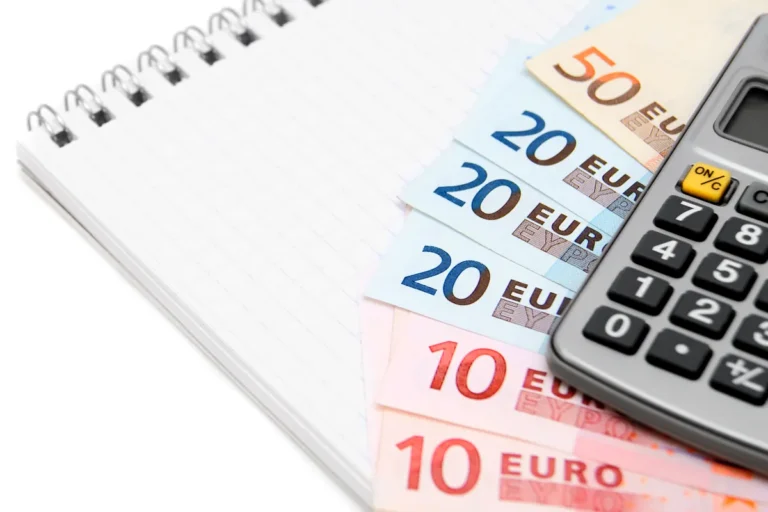 Billets en euros, carnet à spirale et calculatrice posés sur une table blanche