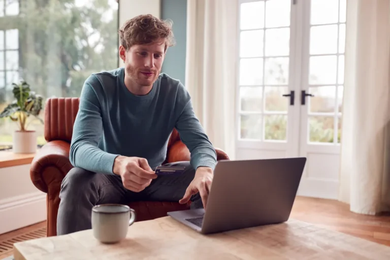 Homme dans un fauteuil en cuir, carte bancaire en main devant son ordinateur portable