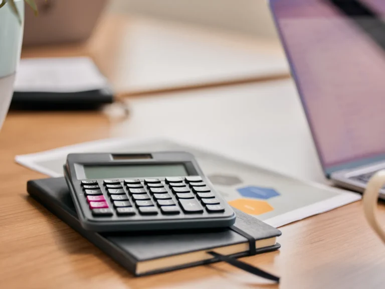 Calculatrice posée sur un carnet noir, à côté de documents avec graphiques et d’un ordinateur portable